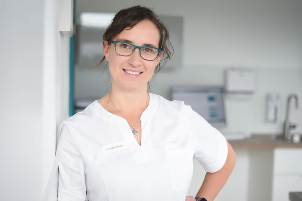 Portrait of Dr Katja Häusler, owner of Kleintierpraxis Cremlingen, smiling, wearing blue glasses.